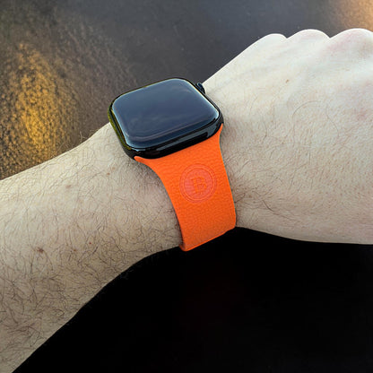 Apple Watch Armband in Orange am Handgelenk getragen mit sichtbarem Bitcoin BTC Logo auf der Vorderseite