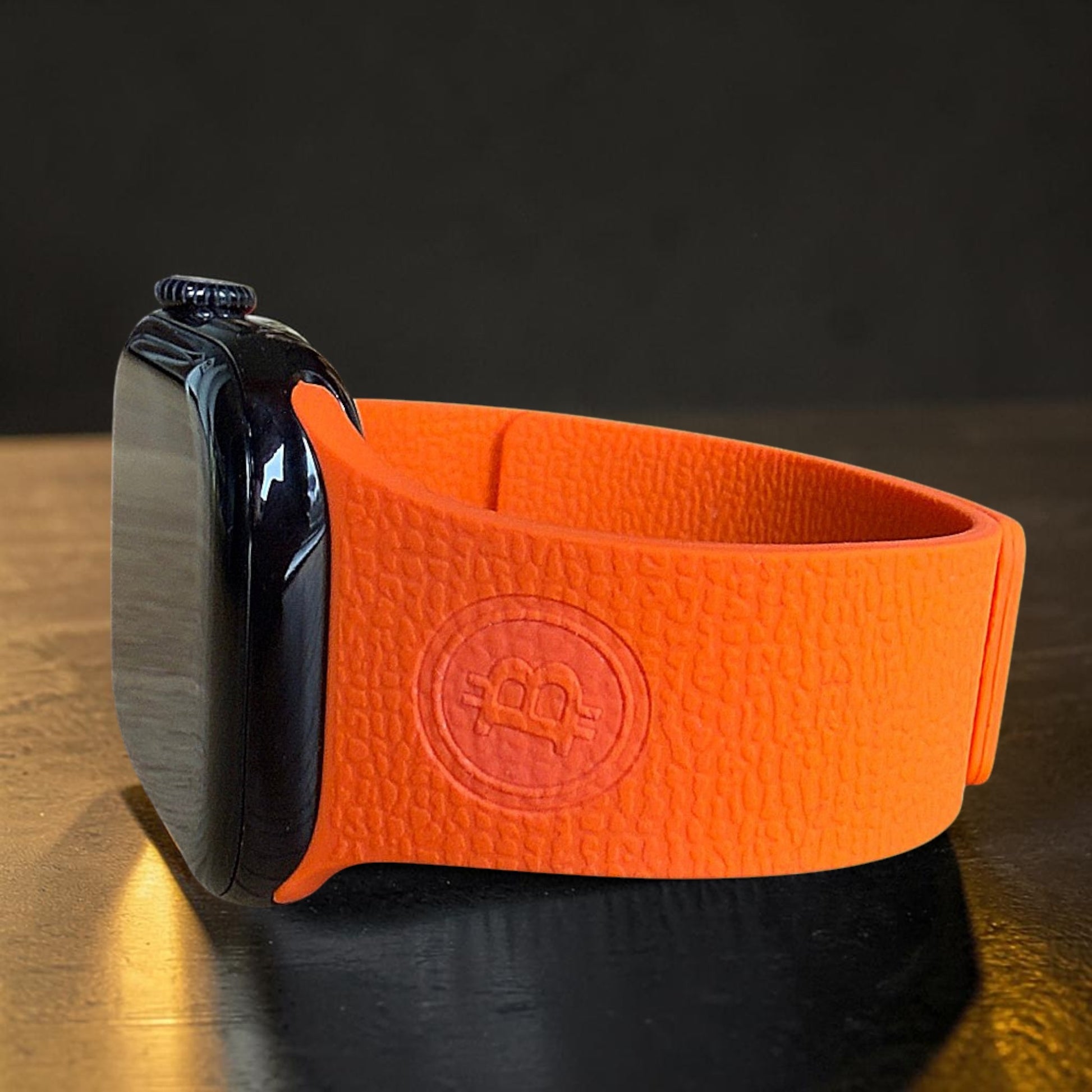 Nahaufnahme eines orangefarbenen Apple Watch Armbands mit geprägtem Bitcoin BTC Logo im Silikon
