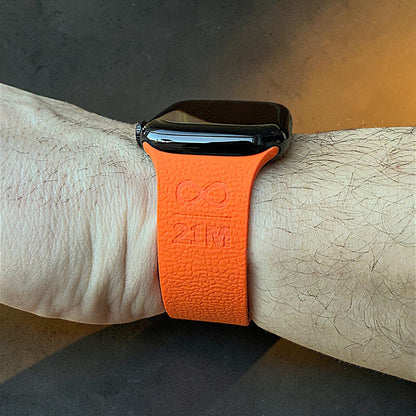 Rückansicht eines orangefarbenen Apple Watch Armbands am Handgelenk mit 21M Symbol Prägung