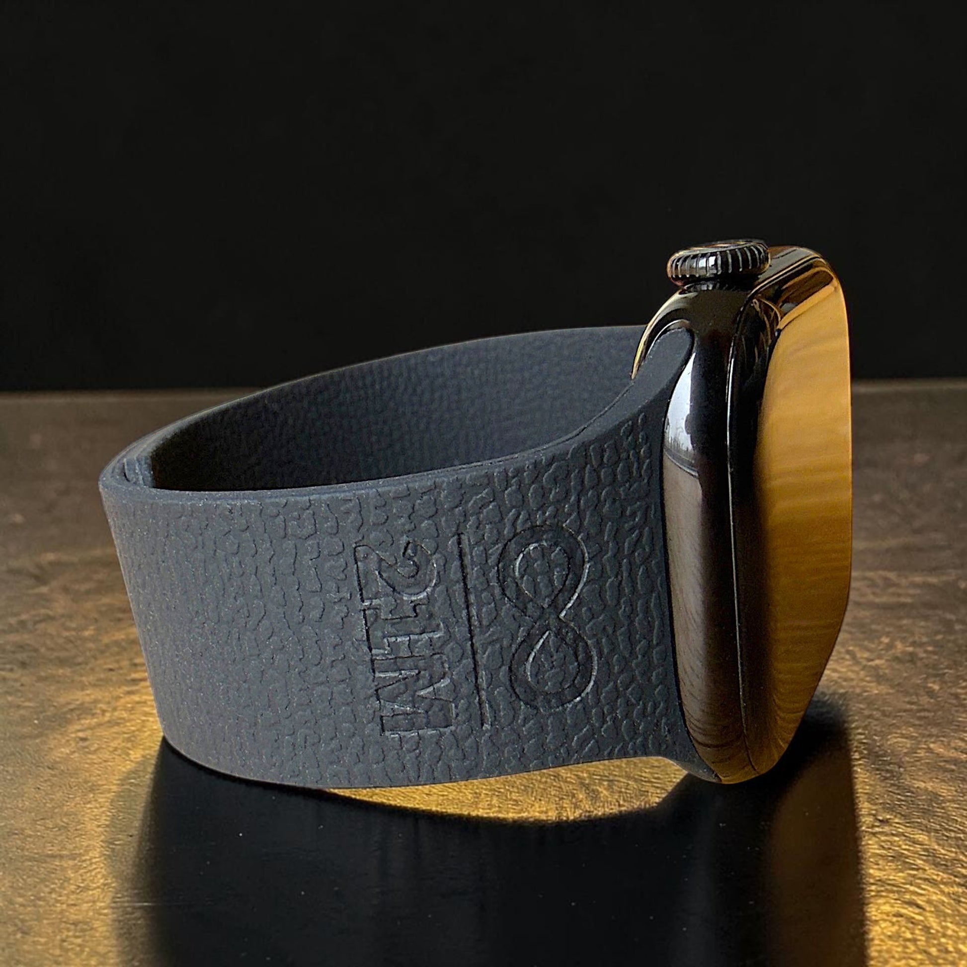 Detailaufnahme eines schwarzen Apple Watch Silikonarmbands mit 21M Symbol Prägung, liegend fotografiert