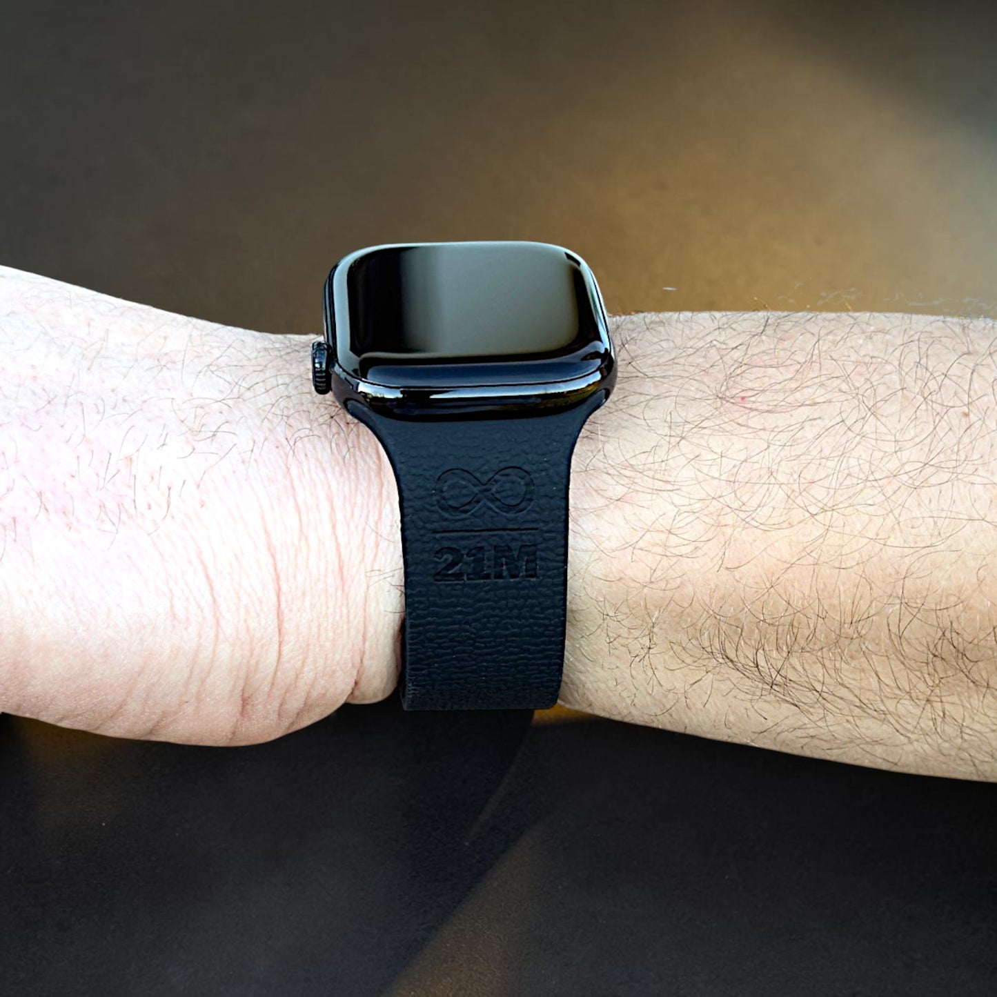 Rückansicht eines schwarzen Apple Watch Armbands am Handgelenk mit 21M Symbol Prägung