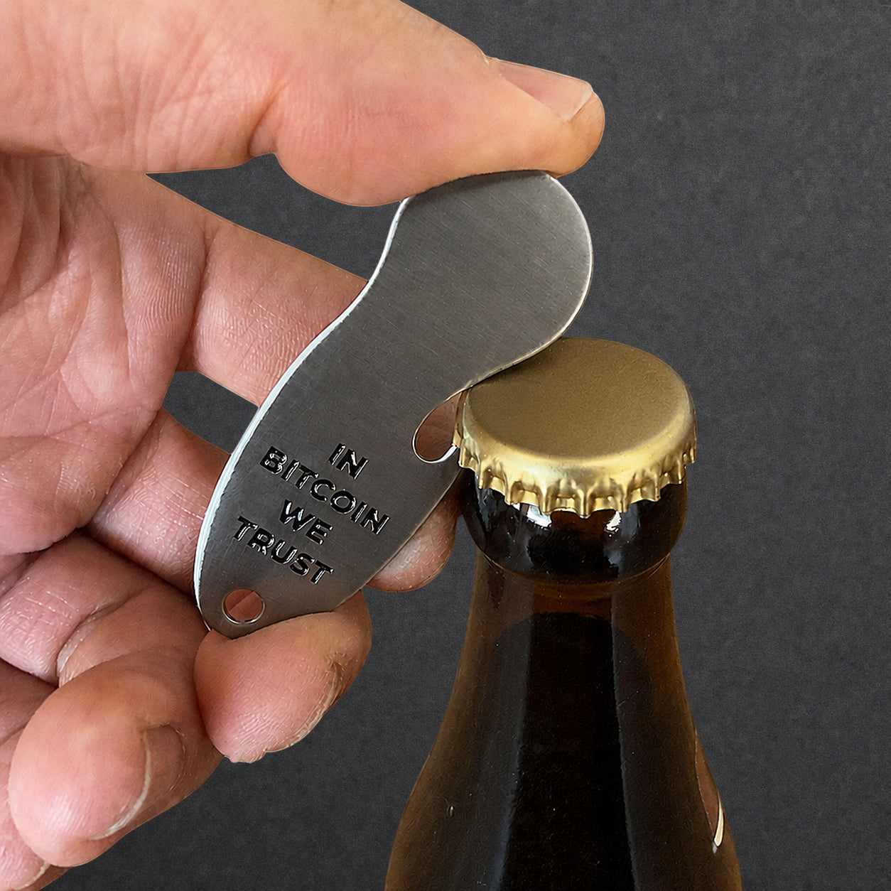 Bitcoin Einkaufswagenlöser in Edelstahl Optik wird als Flaschenöffner zum Öffnen einer Getränkeflasche verwendet