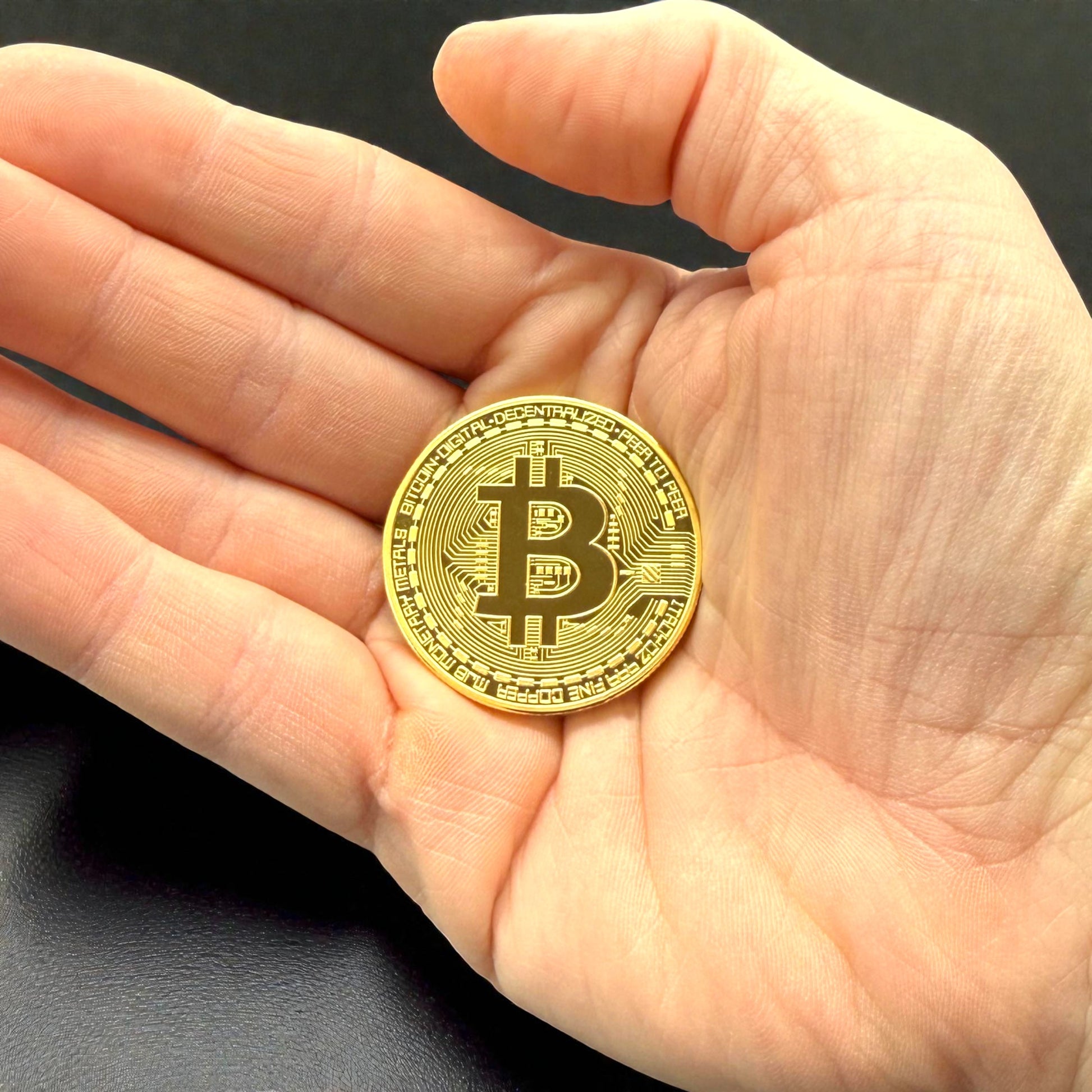 Goldene Bitcoin Münze in der Hand als Größenvergleich